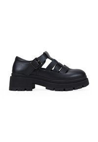 Zapatos de plataforma de cuero negro con puntera redonda, diseño recortado y correa ajustable con hebilla. Suela de goma texturizada con patrón estriado.