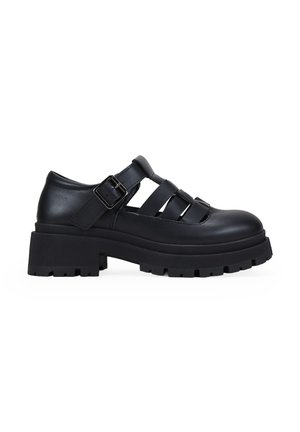 Zapatos de plataforma de cuero negro con puntera redonda, diseño recortado y correa ajustable con hebilla. Suela de goma texturizada con patrón estriado.