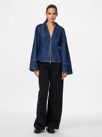 Jeans jakna z zadrgo spredaj, sostavnom ovratnikom in razširjenimi rokavi. Temno modra barva z kontrastnimi šivanji. V kombinaciji s črnimi širokimi hlačami.