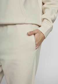 Sudadera y pantalones de color beige claro en una tela suave. Los pantalones tienen un bolsillo lateral; la cinturilla es lisa. Diseño simple y sin costuras, sin patrones.