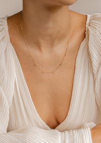 Collana in oro con piccoli accenti distribuiti uniformemente. Design a maglia fine, indossata con un indumento bianco a trama.