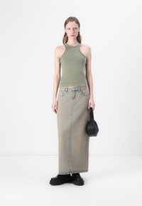 Zeleni halter top u maslinastoj boji uparen s dugom, svijetloplavom traper suknjom. Crne ravne čizme i mala crna torbica za ruku upotpunjuju izgled.
