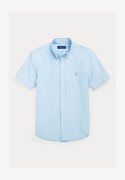 Camisa azul clara de manga curta com botões e colarinho clássico, apresentando um pequeno logótipo bordado no lado esquerdo do peito e barra reta.