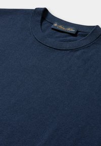 Marineblaues Rundhals-Pullover aus weichem Stoff. Verfügt über eine strukturierte Oberfläche und ein Etikett mit goldener Beschriftung auf dunklem Hintergrund.