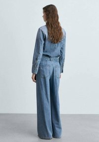 Vaaleansininen farkkupaita ja leveälahkeiset farkut, joissa on napitettu hihansuu ja takataskut, rento istuvuus ja pehmeä rakenne.