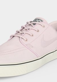 Ανοιχτό ροζ καμβά χαμηλών προδιαγραφών αθλητικό παπούτσι με ταιριαστά κορδόνια, λευκή καουτσούκ σόλα με μαύρη ρίγα και διακριτικό σύμβολο Nike στο πλευρό.