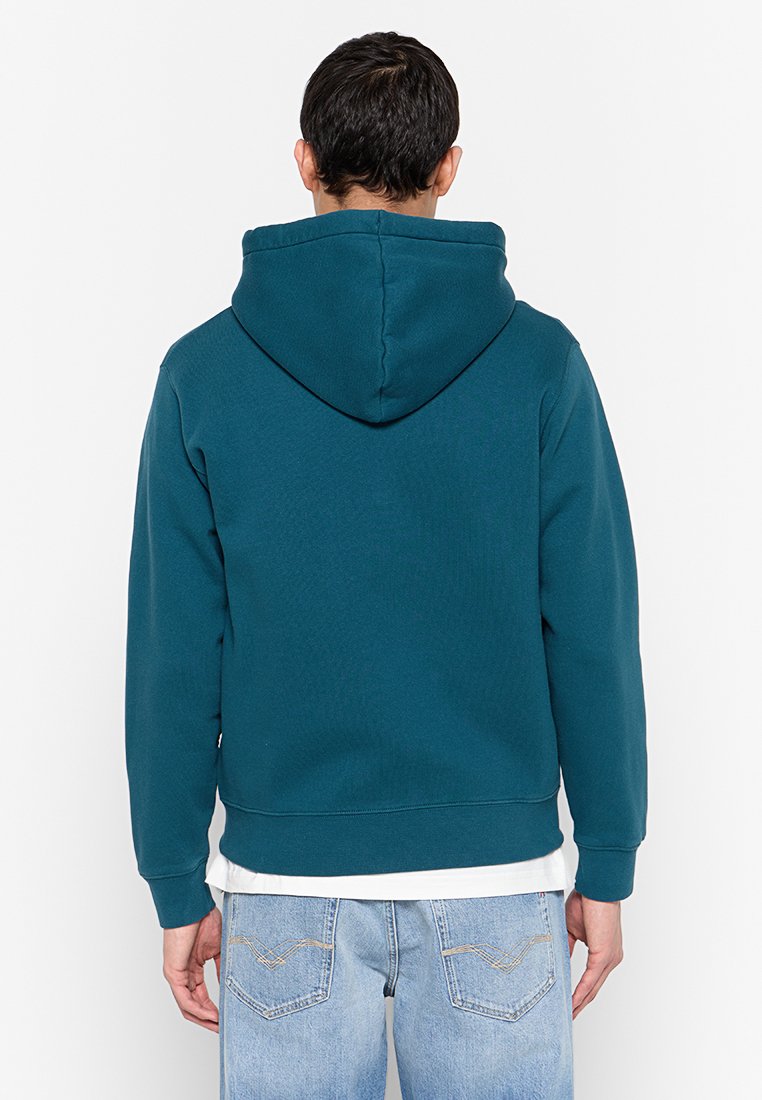 Türkiser Hoodie mit Kängurutasche und Kapuze mit Zugband. Verfügt über gerippte Bündchen und Saum, aus weichem, strukturierter Stoff. Getragen über hellen Jeans.