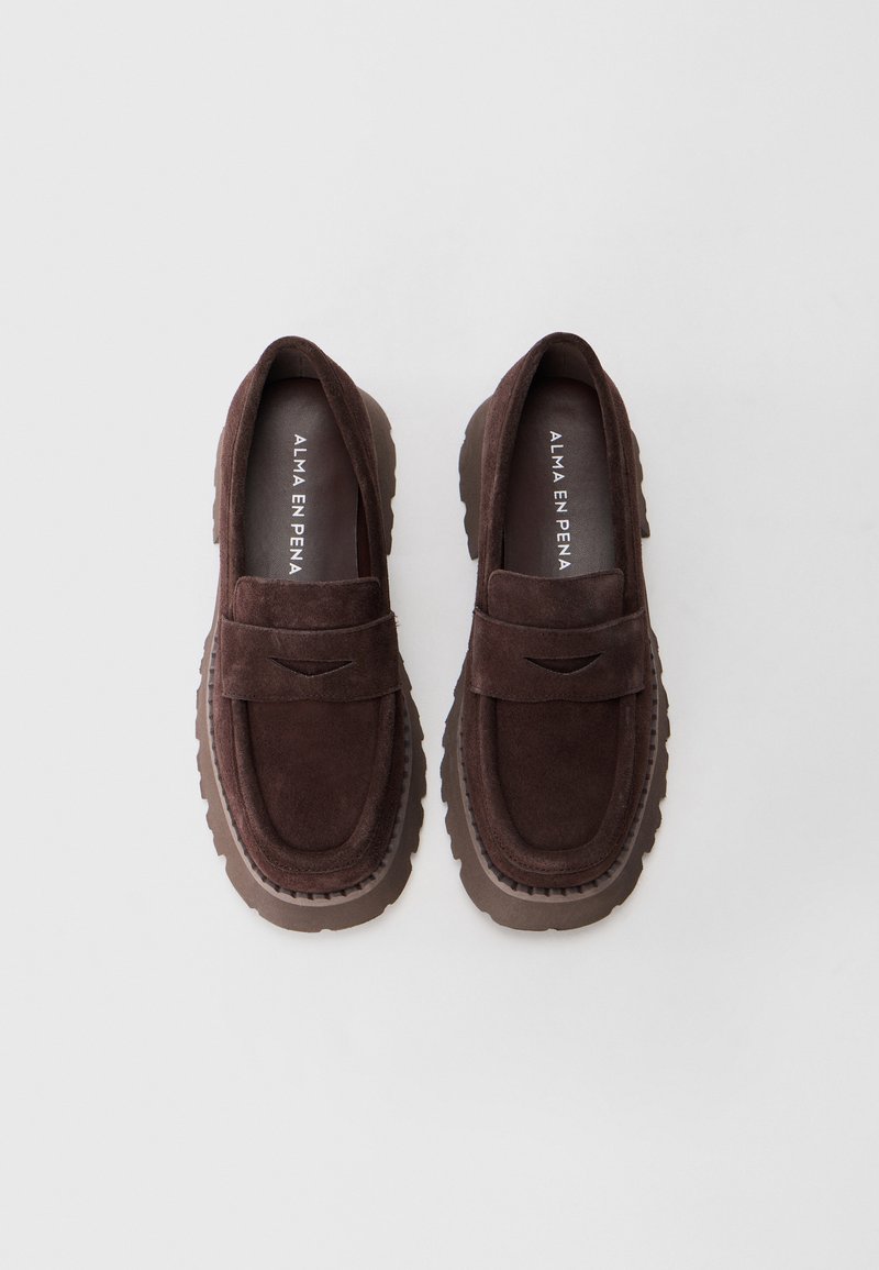 Mocassini in suede marrone scuro con suole spesse e scanalate e una fascia sulla parte superiore, etichettati "ALMA EN PENA" all'interno di ciascun scarpa.