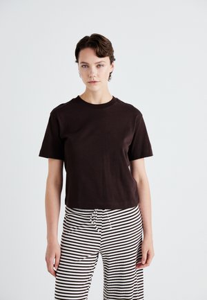 Brun bomulds T-shirt med korte ærmer og rund halsudskæring, som er parret med sort-hvide stribede bukser med elastik i taljen.