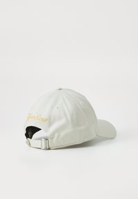 Light grey baseball cap with embroidered “Yankees” in gold, features a curved visor, adjustable strap at the back, and tonal stitching.