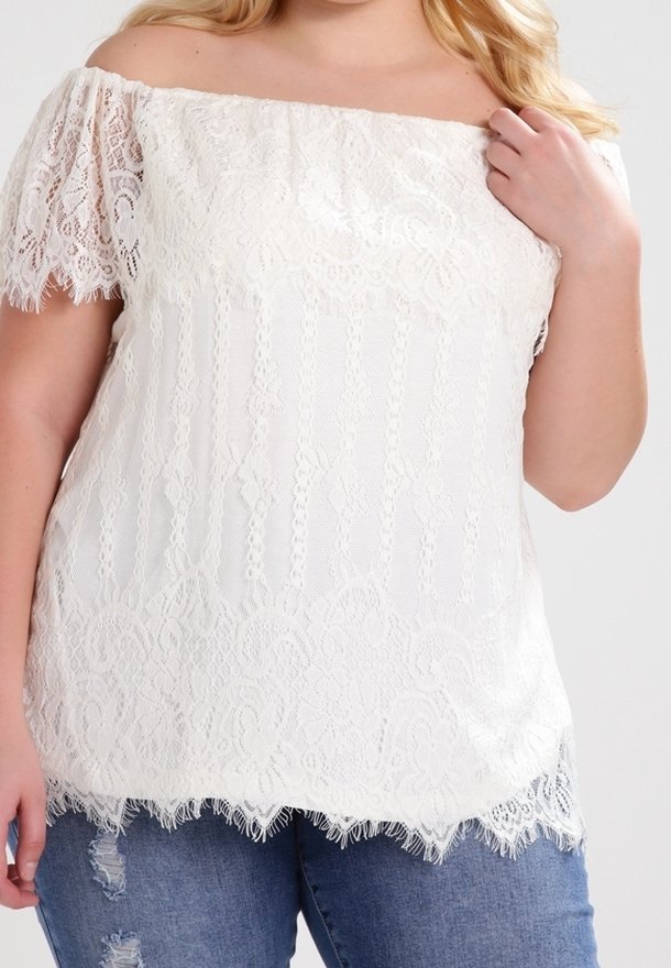 Haut en dentelle blanche à épaules dénudées avec des manches courtes, présentant des motifs complexes et un ourlet festonné. Associé à un jean en denim déchiré.