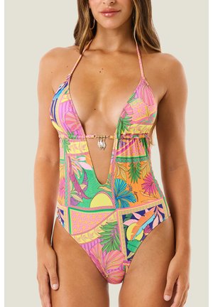 Donna che indossa un costume intero colorato con scollo a V profondo e allacciatura al collo con motivi tropicali e floreali, con dettaglio centrale a chiusura dorata.