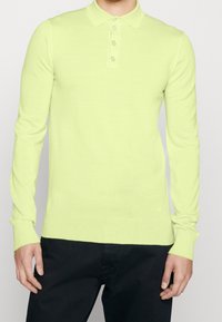 Dlouhý rukáv polo v jasné žlutozelené barvě, s klasickým límcem a čtyřmi knoflíky, vyrobený z hladké pleteniny.