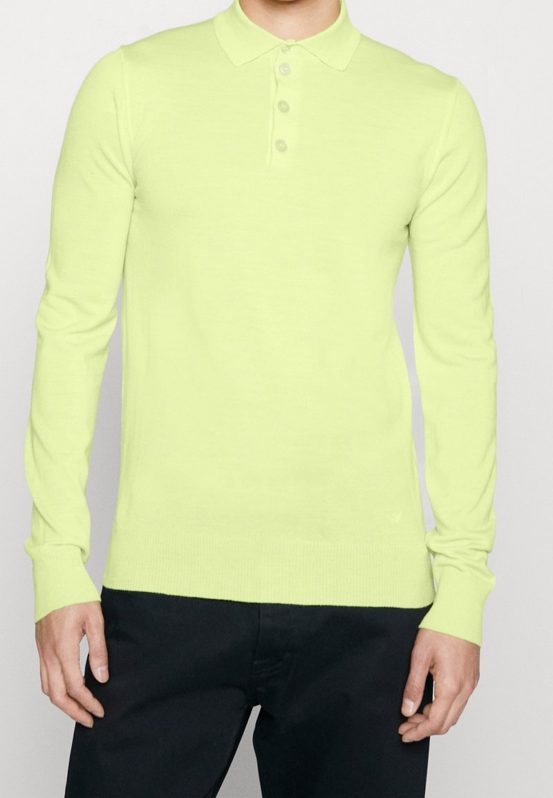 Dlouhý rukáv polo v jasné žlutozelené barvě, s klasickým límcem a čtyřmi knoflíky, vyrobený z hladké pleteniny.