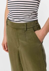 Pantalones de algodón verde oliva con una textura suave, con bolsillos laterales y un diseño de corte recto. Combinados con una blusa de rayas en blanco y negro.