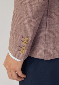 Manche de blazer à carreaux marron avec quatre boutons marron clair. Tissu doux avec une finition texturée. Poignet boutonné révélant une chemise bleu clair.