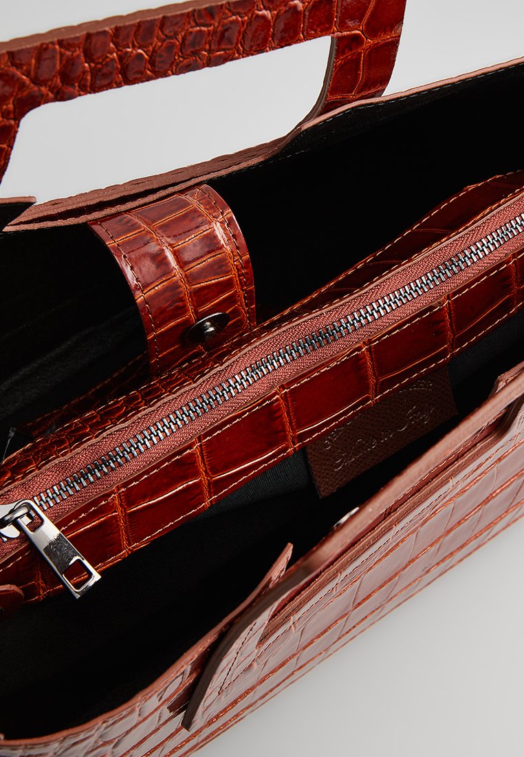 Sac à main marron avec embossage crocodile et finition brillante, doté d'un compartiment zippé et d'un intérieur noir contrastant. Les poignées sont texturées.