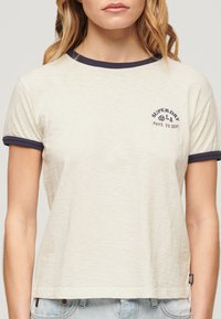 Cremefarvet T-shirt med marineblå ringkanter, der har et logo trykt på brystet. Blødt stof og en afslappet, casual pasform.
