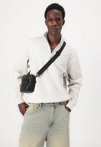 Hanorac gri cu fermoar și mâneci lungi, blugi din denim albastru deschis, și o geantă mică neagră tip crossbody cu o curea unică și închidere cu fermoar.