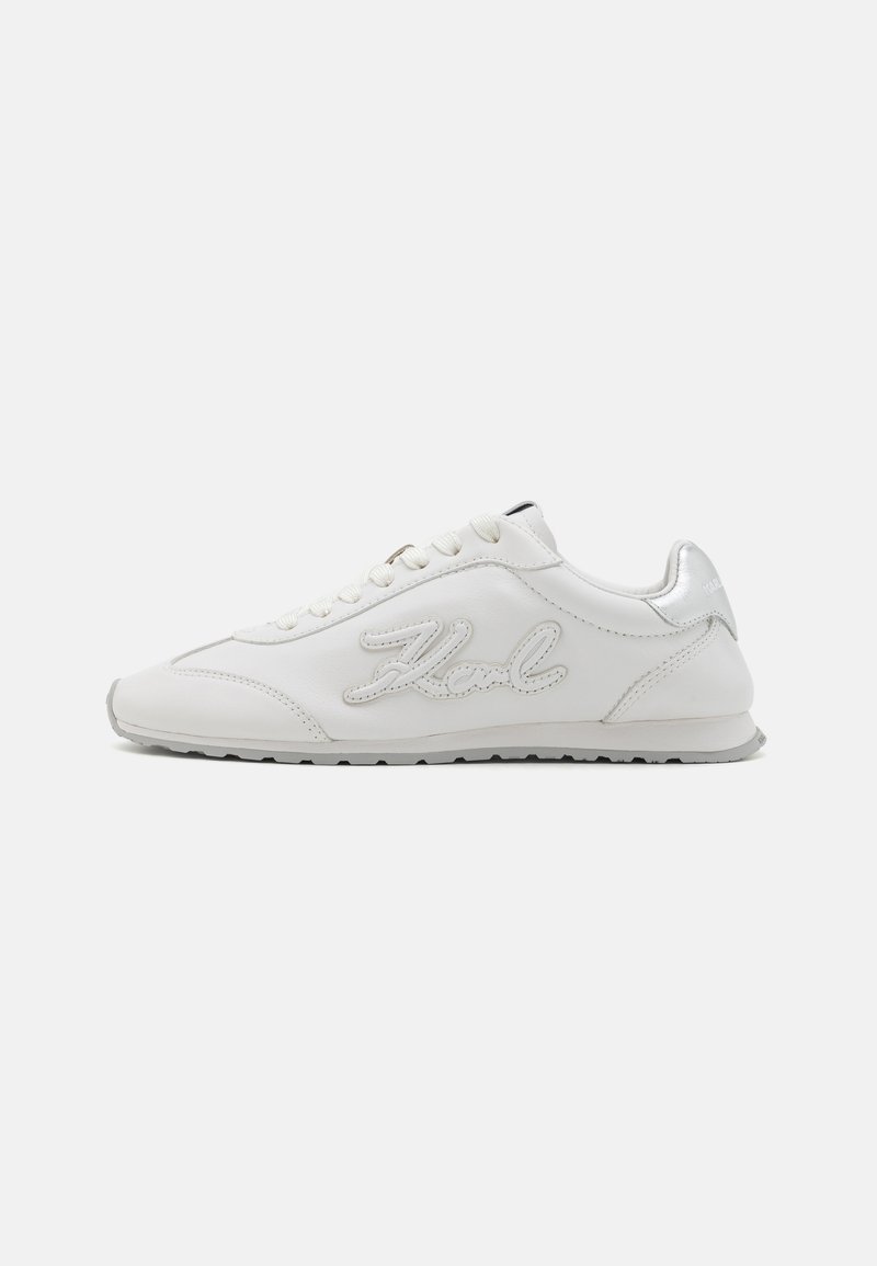 Hvite lær sneakers med en jevn tekstur, sølvdetaljer på hælen og logo i kursiv på siden. Lav profil design.