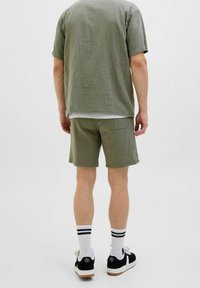 Olijfgroen shirt met korte mouwen en bijpassende shorts van een gestructureerde stof. Draag het met zwarte sneakers en witte sportsokken met zwarte strepen.