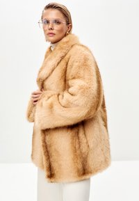Faux fur frakke i lys beige med en blød tekstur, oversized form og klippet krave. Har en afslappet pasform og bløde, voluminøse ærmer.
