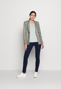 Blazer de cuadros gris de doble botonadura sobre un top de pico azul claro, combinado con jeans skinny oscuros y zapatillas blancas.