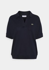 Mörkblå polotröja med korta ärmar, klassisk krage och en broderad grön krokodil-logotyp på vänster bröst. Mjuk tygtextur.