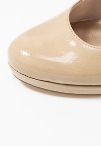 Scarpe flat in pelle verniciata beige, con punta arrotondata, texture liscia e una leggera lucentezza. Presentano un profilo basso e una soletta imbottita.
