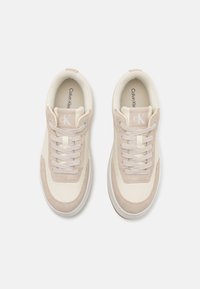 Calvin Klein sportbačiai su kreminės ir šviesiai beige spalvų deriniu, pasižymintys lygiu oda ir zomša, su apvaliu pirštu ir raištelių užsegimu.