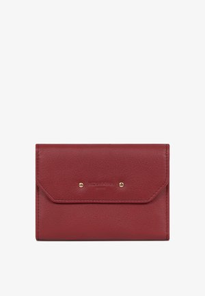 Petit portefeuille rectangulaire en cuir rouge avec un rabat avant sécurisé par deux clous dorés et le nom de la marque discrètement embossé.