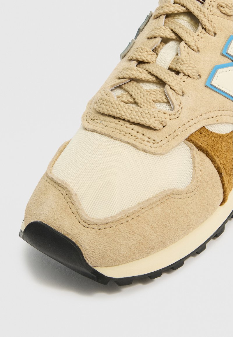 Tan-Suede- und cremefarbene Mesh-Sneaker mit beigen Akzenten und blauen Details. Strukturiert Oberfläche; flache schwarze Gummisohle. Schnürdesign.