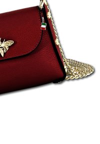 Rode leren handtas met een gouden bij-embleem, voorzien van een gouden kettingband en een klein Italiaans vlaggetje charm. Gestructureerd, met een gladde textuur.