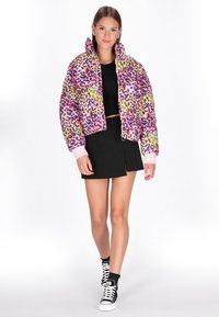 Színes leopárd mintás puffertéli dzseki magas gallérral, cipzáros záródással és rugalmas mandzsettákkal, fekete cropped toppal és szoknyával párosítva.