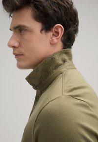 Olijfgroene polo met een textuur, gemusterde kraag; voorzien van knoopsluiting en een getailleerd design; gladde stof en op maat gemaakte vorm.