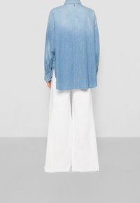 Světle modrá denimová košile s dlouhými rukávy, sklopeným límcem a bočními rozparky, v kombinaci s bílými širokými kalhotami. Žádné viditelné detaily nebo vzory.