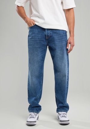 Blue denim jeans with a relaxed fit, featuring a mid-rise waistband and faded areas, paired with white sneakers.