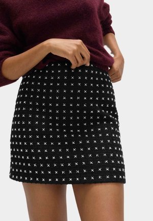 Black mini skirt with a textured woven pattern, featuring small white cross designs. Paired with a burgundy sweater.