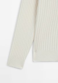 Pull crème à manches longues avec un motif côtelé vertical et des poignets et un bas côtelés, présenté sur fond blanc.