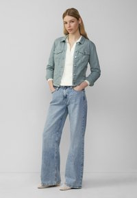 Lichtblauwe denimjacket met een cropped design en zilveren hardware, gecombineerd met loszittende lichtgewassen jeans en een witte top.