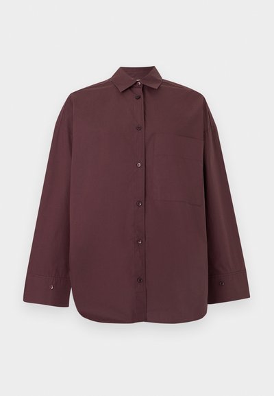 Chemise à manches longues boutonnée de couleur marron foncé avec un col et une unique poche poitrine, présentée sur un fond clair uni.