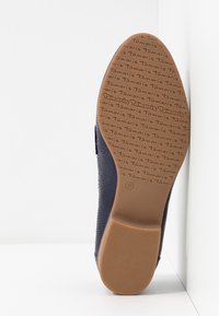 Semelle d'une chaussure bleu marine avec motif texturé, marquée "Tamaris" répétée sur la semelle en caoutchouc marron, taille 37 indiquée près du talon.