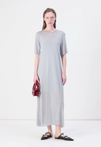 Robe longue gris clair avec des manches courtes, une coupe décontractée et une texture lisse. Associée à des chaussures plates noires et un petit sac à main rouge.