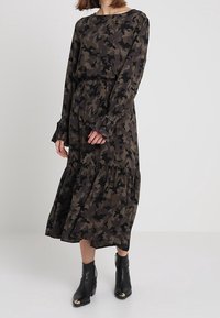 Långärmad kamouflagedress i mörkgrön och svart, med en lager-på-lager kjol och volangärmar, bärs med svarta ankelboots.