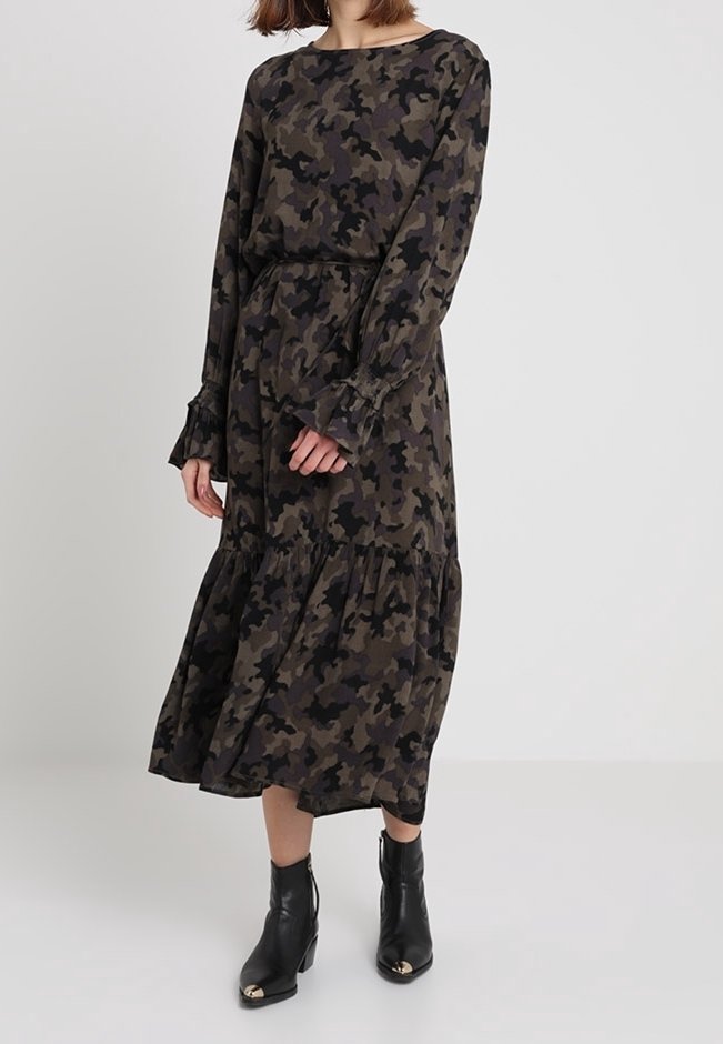 Långärmad kamouflagedress i mörkgrön och svart, med en lager-på-lager kjol och volangärmar, bärs med svarta ankelboots.