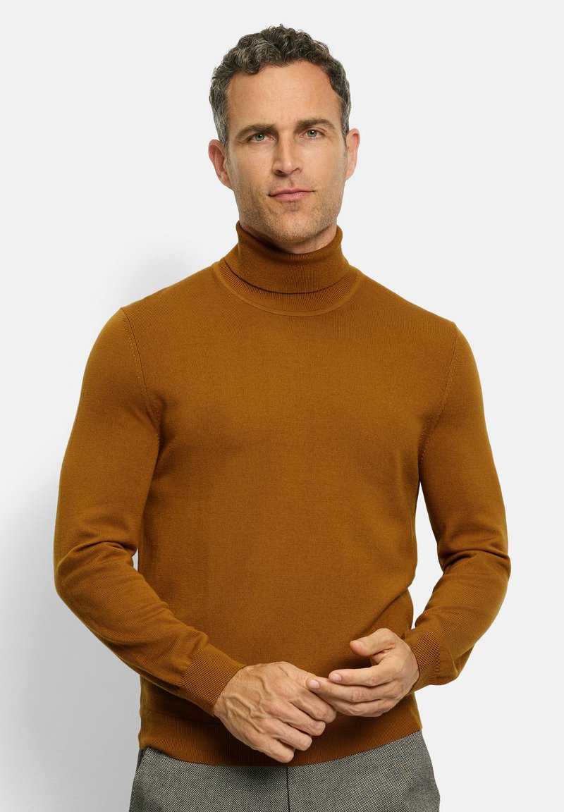 Brauner Rollkragensweater aus strukturiertem Strick, mit langen Ärmeln, taillierter Passform und geripptem Halsausschnitt sowie Bündchen. Das Modell hält die Hände vor sich.