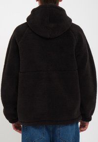 Veste en polaire noire avec capuche, dotée d'une surface texturée et douce ainsi que d'une coupe décontractée. Couture visible traversant le dos pour plus de détails.