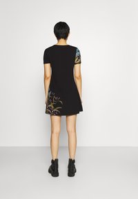 Czarna krótka sukienka z kwiatowymi akcentami na ramionach i u dołu, wykonana z miękkiego materiału. Charakteryzuje się luźnym krojem oraz krótkimi rękawami, zestawiona z czarnymi botkami.