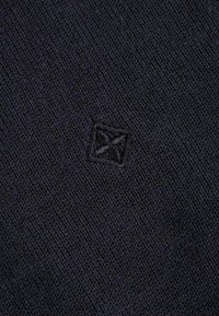 Granatowa dzianina z haftowanym kwadratowym logo, teksturowana powierzchnia z drobnymi detalami. Kompaktowy design o jednolitym kolorze i wzorze.