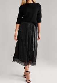 Černý pletený svetr v kombinaci s černou plisovanou sukní s kovovými nitěmi a šedou stužkou v pase. Černé otevřené lodičky.